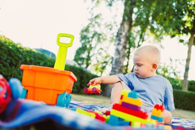 Neşeli bir çocuk neşeli bloklar ve güneşli bir bahçede parlak bir oyuncak kamyonla oynayarak etraflarındaki güzel doğanın yaratıcılığını ve hayal gücünü artırıyor.
