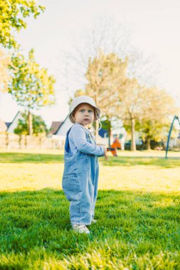 Tulum giymiş neşeli bir çocuk ve güneş şapkası neşe içinde güneşli bir günde yeşil ve neşe dolu bir parkı keşfediyor.