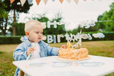 Küçük bir çocuk ikinci doğum günlerini kutlarken dışarıda arkadaşlarıyla ve aileleriyle kutladıkları pastalarına hayran kalarak neşeli bir an yaşanıyor.