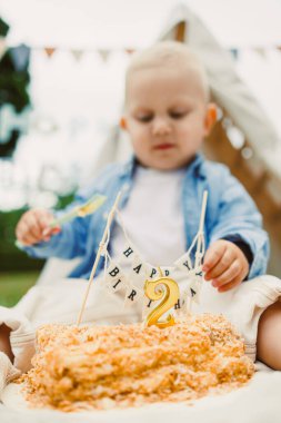 Neşeli bir çocuk, canlı 2. yaş günü partilerinde renkli bir pastanın tadını çıkarıyor, canlı dekorasyonlar, kahkahalar ve sıcak gülümsemelerle çevrili, eğlenceli bir ortam yaratıyor.