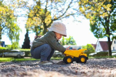 Küçük çocuk dışarıda plastik arabasıyla oyun parkında oynuyor. Bahçede arabasıyla oynayan 2 yaşında tatlı bir çocuk. Çocuk dışarıda yürüyor..