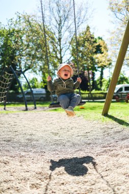 Kafasında Panama şapkası ve salıncakta sallanan açık renk ceketli sevimli 2 yaşında bir çocuk. Parktaki bir çocuk parkında salıncak. Bebek salıncakta sallanıyor. Şık çocuk kıyafetleri..
