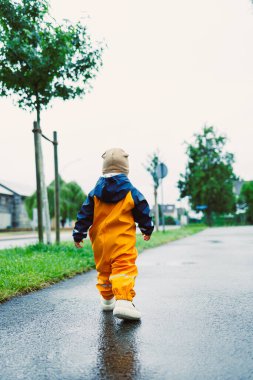 Parlak ve canlı sarı bir yağmurluk giymiş neşeli bir çocuk, yemyeşil yemyeşil bir cadde boyunca mutlu bir şekilde dolaşır, neşeli ve huzurlu bir mutluluk ortamı yaratır.