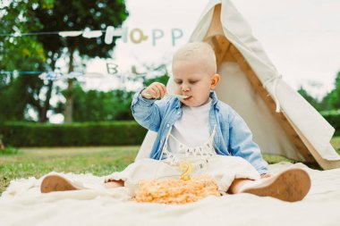 Doğumgünü pastanın tadını çıkaran sevimli bir çocuk. Doğayla iç içe giyinmiş, neşeli bir kutlama anı yakalıyor..