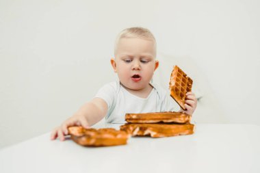 Neşeli bir çocuk modern bir masa ortamında lezzetli waffle 'ları keşfediyor ve eğleniyor, çocukluk sevincinin ve aile anlarının yemek ve yaşam tarzındaki görüntülerini yakalıyor.