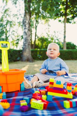 Şirin bir çocuk piknik battaniyesine oturmuş renkli yapı taşlarına odaklanmış, yaratıcılığı ve keşifleri teşvik eden güneşli bir parkta açık havada eğleniyor.