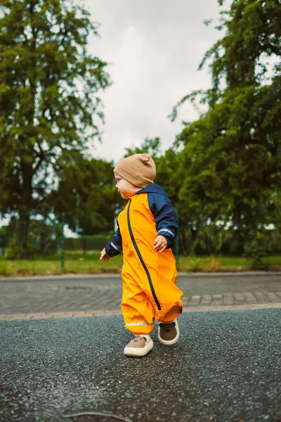 Parlak sarı bir yağmurluk giymiş neşeli, mutlu bir çocuk neşeli bir şekilde kaygan bir yolda yürüyor, çocukluğun kaygısız özünü ve doğayı keşfetmenin heyecanını somutlaştırıyor.
