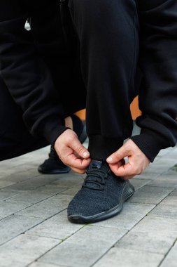 Odaklanmış bir birey ayakkabı bağcıklarını bağlamak için diz çöker ve aktif bir oturuma hazırlanır. Bu sahne fitness ve stil adanmışlığı yakalıyor, kararlılıklarını gösteriyor.