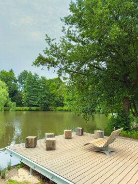 Huzurlu bir ahşap rıhtım manzarası, sakin bir göl, canlı yeşilliklerle çevrili, doğa aşıkları için ideal bir yer yaratıyor.