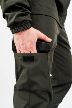 Bir el, açık hava aktiviteleri ve çalışma ortamları için işlevsel tasarımlarını gösteren koyu yeşil yardımcı pantolonun yan cebine bir nesne koyar