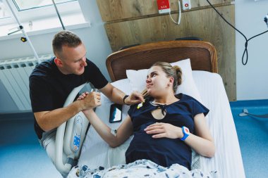 Genç bir çift bir çocuğun doğumu için hazırlanıyor. Kadın doğumhanedeki yatakta yatıyor ve erkek de onu destekliyor. Doğum sırasında kadına destek olmak..