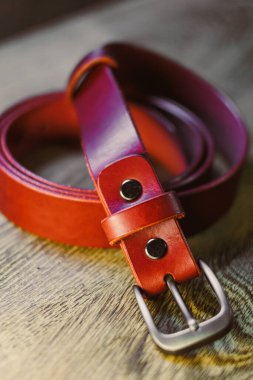 Ahşap bir yüzeye sanatsal olarak yerleştirilmiş gümüş metal tokalı, güzel işlenmiş kahverengi deri bir kemer. Moda ve aksesuar fotoğrafçılığı için mükemmel..