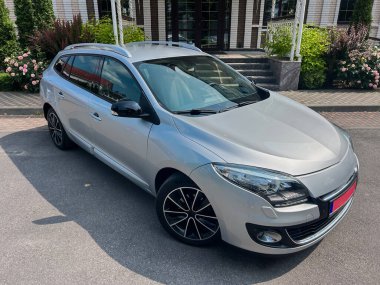 Çağdaş tasarımı, parlak alaşımlı tekerlekleri ve geniş gövdesi, şehir içi sürüş ve aile gezileri için ideal olan parlak gümüş renkli kompakt bir araba caddeye park edilmiştir.