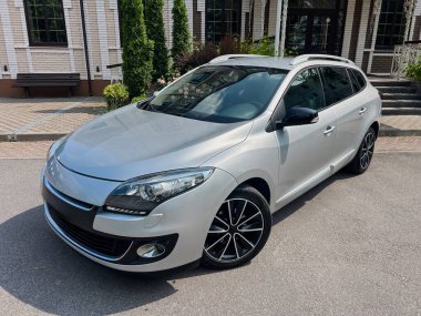 Modern tasarımı klasik bir mimari zemine karşı sergileyen, pitoresk bir ortamda park edilmiş şık, gümüş renkli bir hatchback araba. Otomotiv meraklıları için ideal.