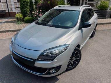 Parlak, gümüş renkli bir hatchback araba, çarpıcı detaylarla modern otomotiv tasarımının güzelliğini ve zarafetini yansıtan açık hava ortamında sergileniyor.