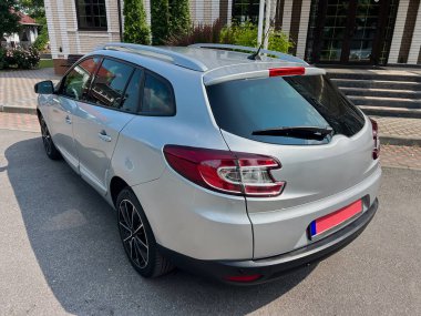 Pürüzsüz ve modern bir tasarıma sahip parlak, gümüş renkli bir hatchback canlı bir şehir ortamında park edilmiş, arka plandaki canlı yeşillik tarafından güzelce tamamlanmış.