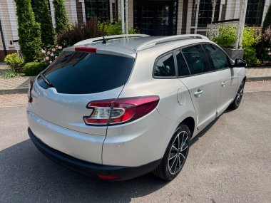 Renkli camları ve siyah alaşımlı tekerleri olan gümüş renkli bir hatchback zarif bir binanın önünde park edilmiş, şehir manzarasında şık tasarımı ve sofistike tasarımı vurgulanıyor.