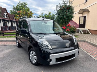 Canlı bir şehir ortamında, parlak siyah renkli bir araba yemyeşil ve renkli çiçeklerin arasına park edilir, yaşam tarzı ve otomotiv stoku görüntülerini yakalamak için mükemmeldir.