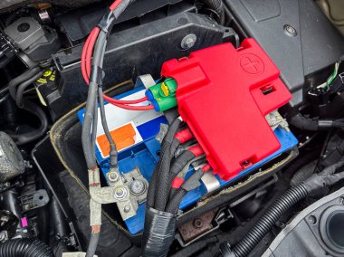 Bu bilgilendirici görünüm tipik bir araba aküsünü ve sigorta kutusunu motor bölmesinde gösterir, gerekli bağlantıları ve otomotiv bakımı için gerekli bileşenleri vurgular