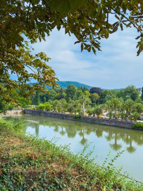 Bereketli ağaçların arasında dolambaçlı bir nehrin huzurlu manzarasının tadını çıkar. Güneşli bir gökyüzü altında rahatlamak, yürüyüş yapmak, piknik yapmak ve güzel manzaralar görmek için güzelliği yansıtıyor.