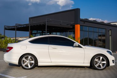 Göz kamaştırıcı ve gösterişli beyaz bir araba modern mimari bir binanın yanında zarif bir şekilde park edilmiş, mükemmel bir şekilde tasarlanmış ve sofistike bir şekilde mavi gökyüzü altında sergilenmektedir.