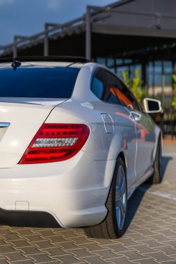 Çarpıcı ve şık bir beyaz coupe, zarif tasarımı ve birinci sınıf özelliklerini vurgulayan sıcak güneş ışığıyla yıkanmış çağdaş bir otoparkta güzelce sergilenir.