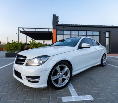 Soluk kesici beyaz MercedesBenz CClass coupe modern bir binanın önünde zarif bir şekilde park edilmiş, herkesin hayran kalacağı lüks tasarımı ve zarafetini sergiliyor.