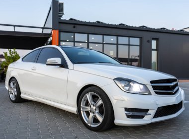 Şık ve şık bir beyaz coupe modern bir binanın önünde zarif bir şekilde park edilir. Lüks tasarımını ve çekici özelliklerini canlı bir şehir zeminine karşı sergiler.