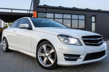 Çarpıcı ve zarif beyaz bir MercedesBenz coupe nefes kesen çağdaş şehir arka planına karşı park edilmiştir. Şık tasarımı ve modern estetiği güzel bir şekilde sergilenmektedir.