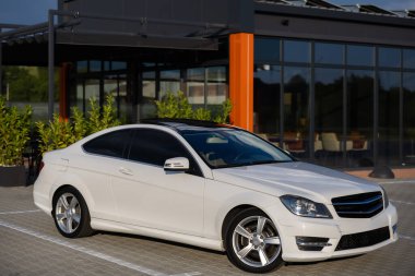 Gösterişli, beyaz bir coupe modern bir cam binanın dışında zarif bir şekilde duruyor. Sportif tasarımı ve şık cazibesiyle.