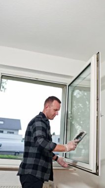 Yakışıklı profesyonel temizlikçi evin camlarını yıkıyor. Temizlik şirketinden bir adam evde plastik camları yıkıyor. Evde profesyonel temizlik var. Temizlik servisi.