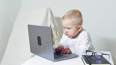 Bebek masada oturuyor ve dizüstü bilgisayar ekranına bakıyor. 2 yaşındaki bir çocuk dizüstü bilgisayarı olan bir ofis çalışanı gibi görünüyor. Çocuk çizgi filmleri dikkatle izliyor..