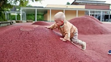 Küçük aktif çocuk oyun parkındaki tepelerde koşuyor. Çocuk koşuyor ve temiz havayı soluyor. Kot pantolonlu ve tişörtlü çocuk dışarıda oynuyor..