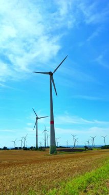 Mavi gökyüzünde dönen rüzgar türbinleri. Rüzgar türbinleri enerji üretiyor. Kırsalda bir yel değirmeni çiftliği var..