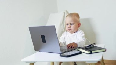 2 yaşında bir çocuk evde bir masada oturuyor ve bir dizüstü bilgisayara bakıyor. Bir çocuk taşınabilir bir bilgisayarda çizgi film izliyor. Modern bir çocuk ve bilgisayar..