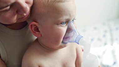 Çocuğun yüzünde maskeyle birlikte terapi amaçlı solunum. Çocuk öksürük ilacıyla nebulizörden nefes alıyor. Çocuğa evde bakılıyor. Evde çocuğun solunumu.