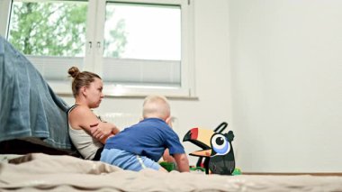 Yorgun bir annenin evde oturduğu ve çocuk oynarken yüzünü ellerle kapattığı manzara. Ebeveynlik sorunları. Kadın doğum sonrası depresyonu.