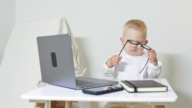Gözlüklü çocuk bilgisayardaki masada oturuyor. Çocuk işadamı evde dizüstü bilgisayarla çalışıyor. Yeni yürümeye başlayan çocuk girişimciyi oynuyor. Ofiste bilgisayarla oynayan bir çocuğun portresi..