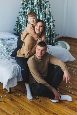 Neşeli bir aile portresi, sevgi dolu bir anne ve küçük oğlunun güzel dekore edilmiş bir Noel ağacında rahatladığını, tatil sezonunu sıcaklıkla ve neşeyle kutladıklarını gösteriyor.