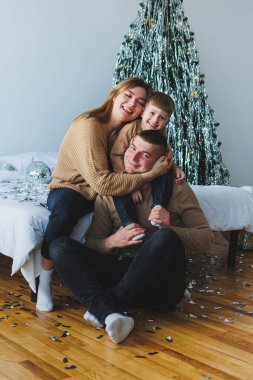 Neşeli bir aile, sevgi ve kahkahalarla dolu sıcak bir atmosferde, çok güzel dekore edilmiş bir Noel ağacı ile iç açıcı bir anı paylaşıyor.