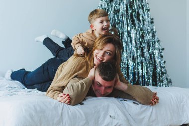 Sevecen bir çocuk sevgi dolu bir ortamda sevgi dolu ebeveynlerin üzerine tırmanır, aile neşesinin, sıcaklığın ve birlikte geçirdikleri zaman boyunca paylaştıkları güzel bağın özünü yakalar.