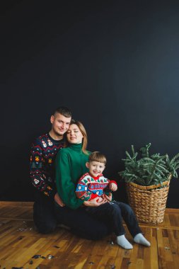 Neşeli bir aile renkli tatil kazaklarıyla birlikte poz verirken, bu şenlik sezonunda sevgilerini ve sıcaklığını sergilerken, yemyeşil bir bitki arka planı süsler.