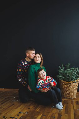 Üç kişilik neşeli bir aile, şen süveter giyip, özel anları ve sıcak kış havasını kutlamak için mükemmel bir tatil atmosferi yaratıyor.