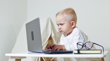 Bebek masada oturuyor ve dizüstü bilgisayar ekranına bakıyor. 2 yaşındaki bir çocuk dizüstü bilgisayarı olan bir ofis çalışanı gibi görünüyor. Çocuk çizgi filmleri dikkatle izliyor..
