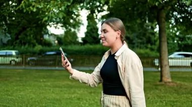 Yazın parkta eğlenirken telefonda konuşan pozitif bir kadın. Akıllı telefondan konuşan sıradan bir kadın doğaya karşı, güneşli bir günün tadını çıkarıyor..