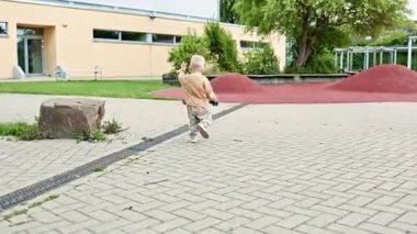 Şehir parkında koşan koşucu ve tişörtlü bir çocuk. Çocuk dışarıda yürürken koşuyor ve eğleniyor. Çocuk gelişimi ve mutlu bir çocukluk. Sokakta yürüyen küçük çocuk.