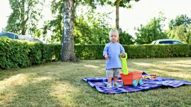 Şortlu ve tişörtlü bir çocuk dışarıda çimde bebek arabasıyla koşuyor. Çocuk arka bahçede oynuyor ve çimlerde koşuyor. Çocukların açık hava oyuncakları.