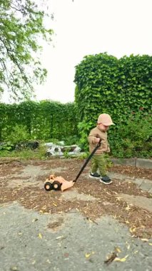 2 yaşında bir çocuk caddede yürüyor ve arkasından plastik bir araba çekiyor. Bir çocuk dışarıda plastik bir arabayla oynuyor. Çocuk gelişimi ve bir bebek için sağlıklı bir yaşam tarzı.