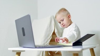 Gözlüklü akıllı 2 yaşındaki çocuk evdeki masada dizüstü bilgisayar kullanıyor. Çocuk uzaktan öğrenme sırasında bilgisayarın başında oturur. Çocukluk ve modern teknolojiler.