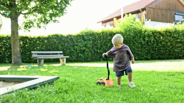 Tişörtlü ve şortlu bir bebek. Çocuk kumda plastik bir arabayla oynuyor. 2 yaşındaki küçük bir çocuk oyun parkındaki kum havuzunda oynuyor. Bebek kum küreğiyle oynuyor..